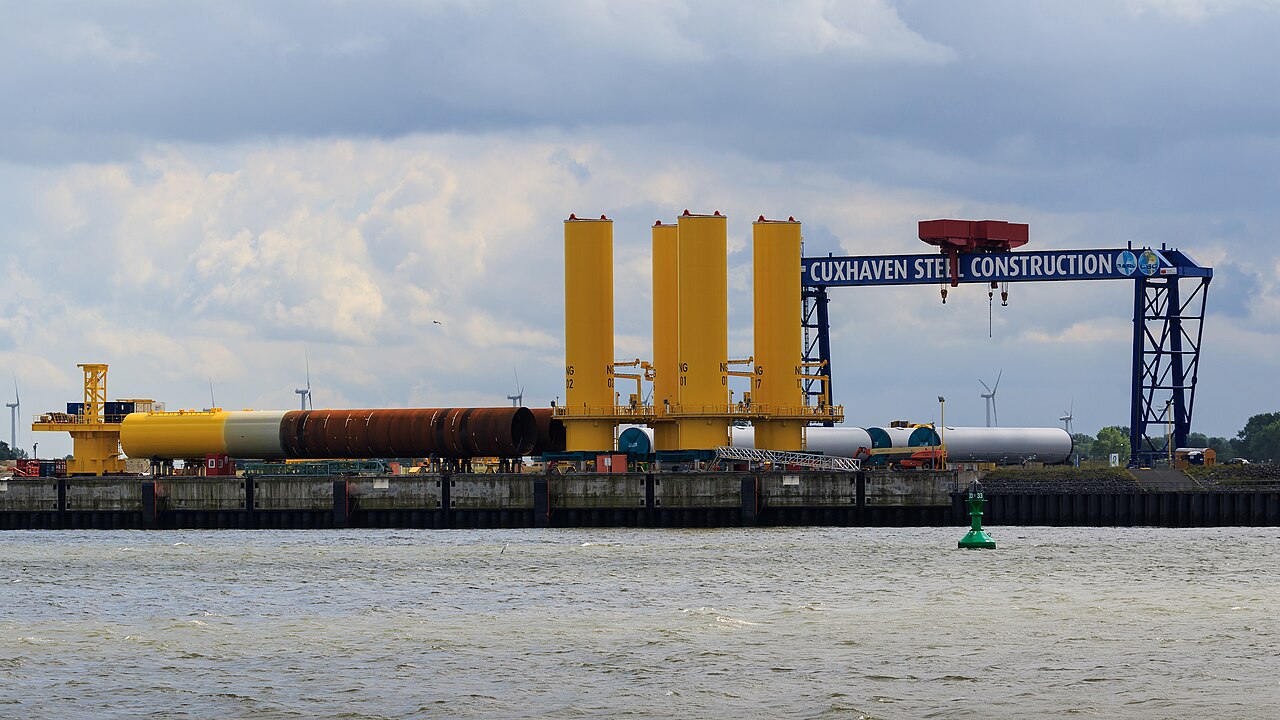 Offshore wind foundation components beside a large fabrication crane at Cuxhaven